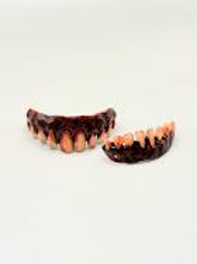 May include: Two sets of prosthetic teeth featuring a dark, blood-stained gum appearance with uneven, yellowish-toned individual teeth. The dental appliances are curved to fit a mouth, displaying a realistic, aged, and decayed aesthetic for costume use.