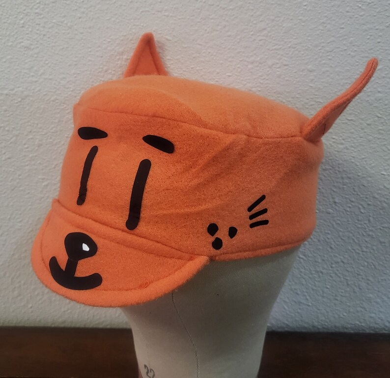 May include: Orange felt hat with black cat ears and a black cat face with eyes, nose, and whiskers.