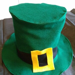 May include: A green felt leprechaun hat with a black band and a yellow buckle. The hat has a tall, cylindrical crown and a wide brim.