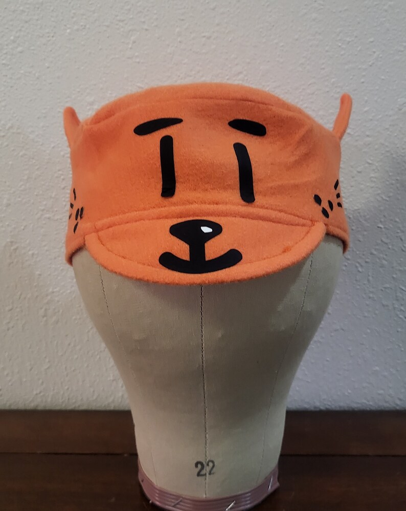 May include: Orange fleece hat with a black cartoon face on the front. The face has two eyes, a nose, and a mouth.