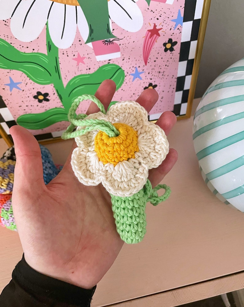 Op de afbeelding: Een gehaakte bloem met een gele kern en witte bloemblaadjes bevestigd aan een groene stengel. De bloem is handgemaakt en zou een geweldig cadeau zijn.