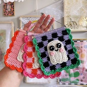 May include: A collection of handmade crochet banners in various colors, including pink, orange, and purple. One banner features a smiling ghost design. Each banner has a scalloped edge and is suspended by a black and white string.