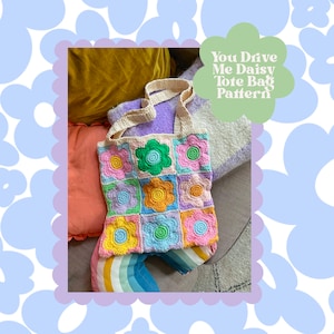 May include: A crocheted tote bag with a daisy pattern in various colors, including pink, yellow, green, and blue. The bag has a cream-colored handle and the text "You Drive Me Daisy Tote Bag Pattern" on a green background.
