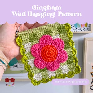 Könnte beinhalten: Handgefertigter Wandbehang aus Häkelarbeit mit einem Vichy-Muster in Grün und Weiß, mit einer großen rosa und orangefarbenen Blume. Der Text "Gingham Wall Hanging Pattern" steht oben. Die Kanten sind gewellt und grün eingefasst.
