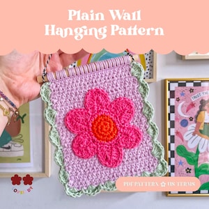 Könnte beinhalten: Gehäkelter Wandbehang mit einem rosa Blumendesign. Das quadratische Stück hat einen hellvioletten Hintergrund, eine leuchtend rosa Blume mit orangefarbenem Zentrum und einen grünen, gewellten Rand. Der Text "Plain Wall Hanging Pattern" steht oben.
