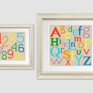 Puede incluir: Dos piezas de punto de cruz enmarcadas, una con el alfabeto en colores arcoíris y la otra con los números del 1 al 10 en colores arcoíris.