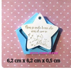 Può includere: Uno stampo in silicone blu a forma di stella con una stella bianca al suo interno. La stella bianca contiene una citazione in italiano che dice "Non si vede bene che con il cuore" e una piccola illustrazione di un personaggio con una volpe. Lo stampo misura 6,2 cm per 6,2 cm per 0,5 cm.