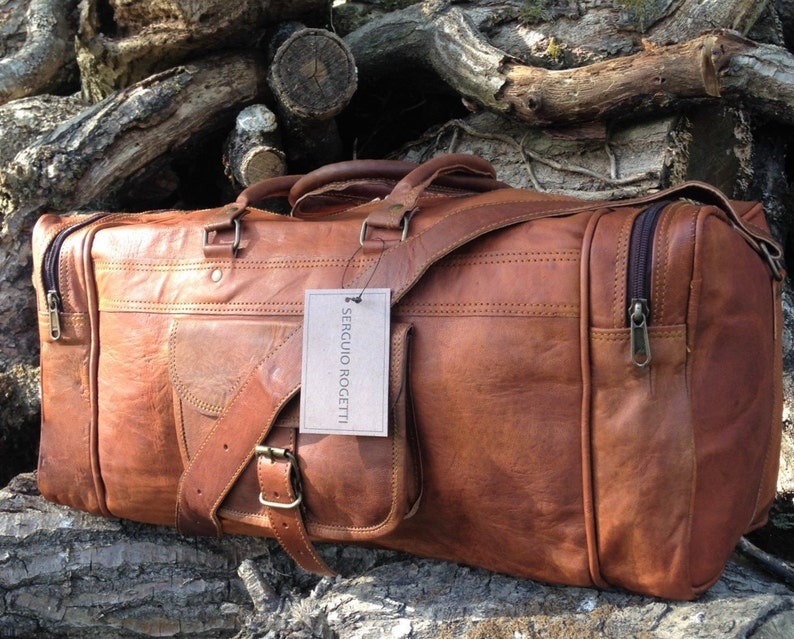 May include: A brown leather duffel bag with a shoulder strap and a zippered pocket. The bag has a label that says "Sergio Rocetti".