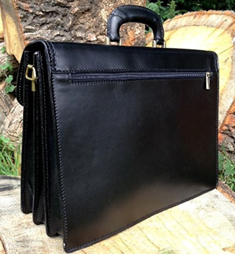 May include: Black leather briefcase with a top handle and a zippered pocket. The briefcase has gold-colored hardware and a structured design. The stitching is visible along the edges, and the briefcase appears to be made of high-quality leather.
