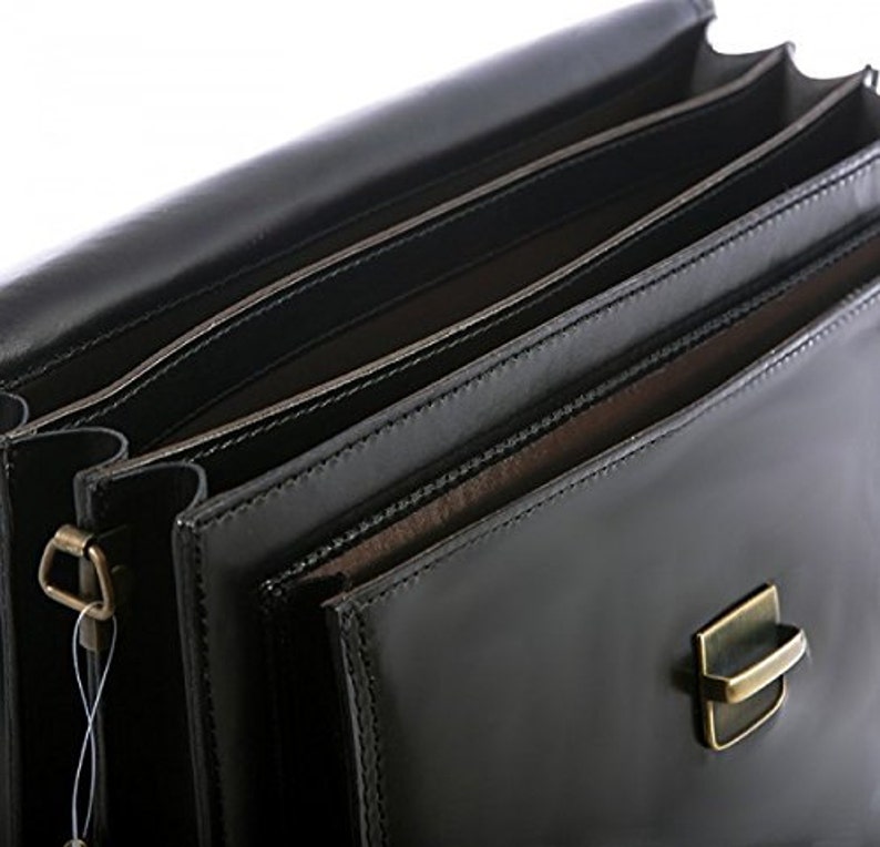 May include: A close-up of a black leather briefcase with multiple interior compartments. The briefcase has a shiny finish and a metal clasp. The interior appears to be lined with a lighter brown material. The briefcase is designed for carrying documents and other professional items.