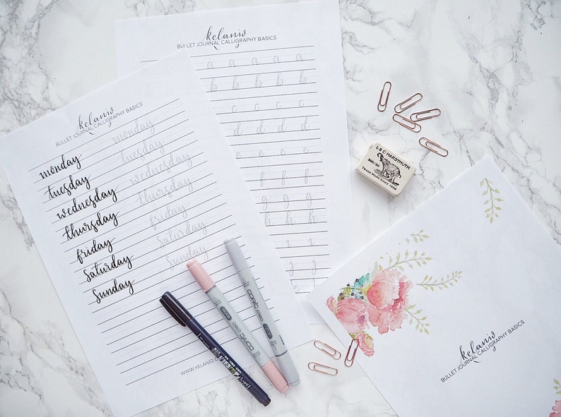 May include: Two printable worksheets for bullet journal calligraphy basics. The worksheets feature a list of days of the week and the alphabet. The worksheets are on a white background with gray lines. There are three black and pink markers and a pink eraser on the worksheets.