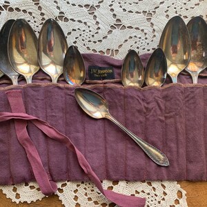 May include: A set of silver spoons in a purple fabric roll with the text "J.W. Johnson New York" on the roll.