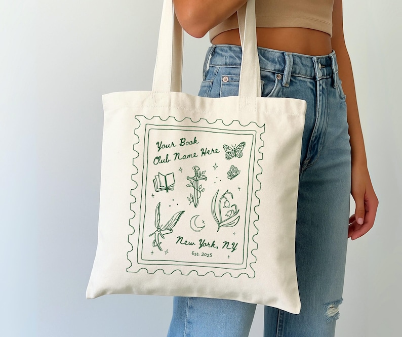 May include: Cream-colored tote bag with a green stamp-like design. The design includes a book, a sword, butterflies, and botanical illustrations. Text on the bag reads "Your Book Club Name Here" and "New York, NY Est. 2025".
