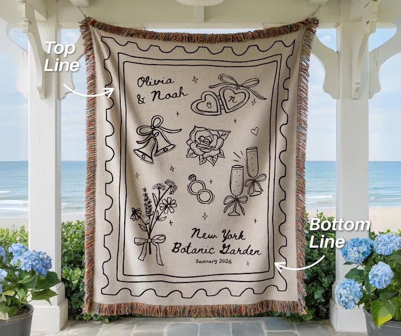 May include: Beige throw blanket with black line art of wedding-themed illustrations, including hearts, bells, and flowers. The text reads "Olivia & Noah" and "New York Botanic Garden January 2026". The blanket has a fringed edge.
