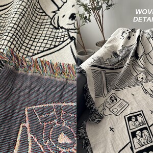 May include: Woven throw blanket with black and white illustrations of dogs, buildings, and other graphics. The blanket has a fringed edge with colorful threads. The words "WOVEN DETAILS" are visible in the upper right corner.