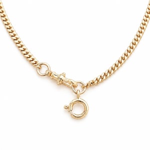 Op de afbeelding: Een goudkleurige gourmetketting met een gepolijste afwerking. De ketting is verbonden met een metalen draaibare karabijnsluiting, die is bevestigd aan een ronde veerringsluiting. Het ontwerp toont een klassiek patroon van in elkaar grijpende schakels.