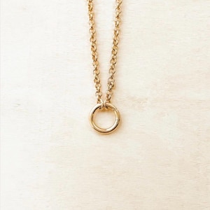 May include: A gold-toned necklace featuring a thick, round link chain that connects to a circular pendant. The pendant is a simple, smooth gold-toned ring that hangs vertically from the chain, creating a clean and uniform metallic appearance.