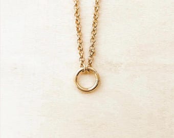 May include: A gold-toned necklace featuring a thick, round link chain that connects to a circular pendant. The pendant is a simple, smooth gold-toned ring that hangs vertically from the chain, creating a clean and uniform metallic appearance.