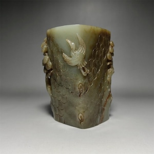 May include: A green jade cup with intricate carvings of a bird and floral designs. The cup is made of a smooth, polished jade and has a slightly rounded shape.