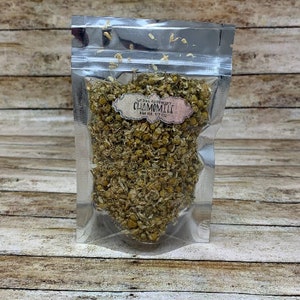May include: A silver resealable pouch filled with dried chamomile flowers. The pouch has a label that reads "The Herb Sanctuary Chamomile 1 oz (28 g)"