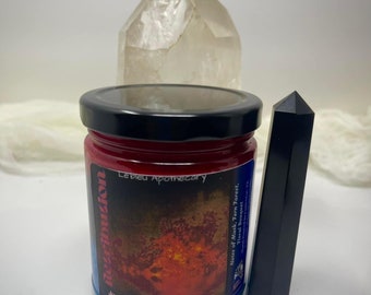 May include: A red glass jar with a black lid and a label that reads "Revolution" and "Justice | Revenge | Punishment". The jar is filled with a red substance and has a white background with the words "Le bleu Apothecary" and "Notes of Musk, Fern Forest, Floral Bouquet" on the label.