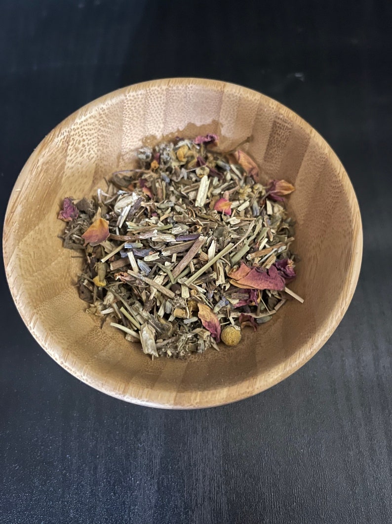 May include: A wooden bowl filled with a blend of dried herbs and flowers, including rose petals, chamomile, and lavender.