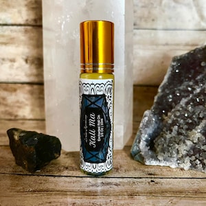 May include: A gold roller bottle with a blue and white label that says "Kailma Enchanted Roll On 1/3 oz | 10 ml".