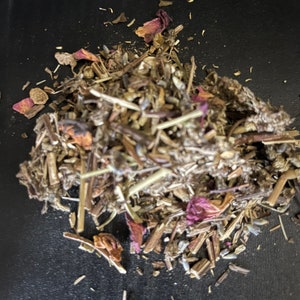 May include: A close-up of a pile of dried herbs and flower petals, including lavender, rose, and other botanicals. The herbs are a mix of brown, green, and purple.