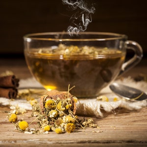 May include: A steaming cup of chamomile tea with dried chamomile flowers scattered on a wooden table.