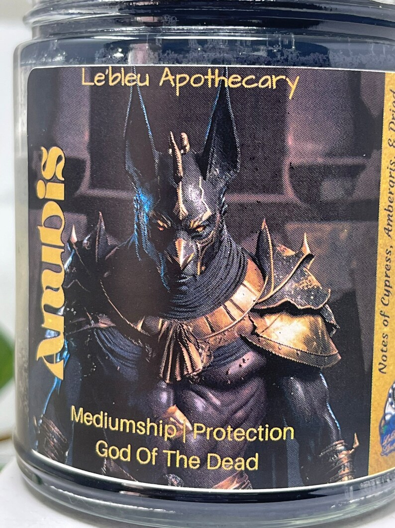 May include: Black and gold candle jar with an image of Anubis, the Egyptian god of the dead. The label reads "Anubis Mediumship | Protection God Of The Dead" and "Le'bleu Apothecary". Notes of Cypress, Ambergris, & Priad.