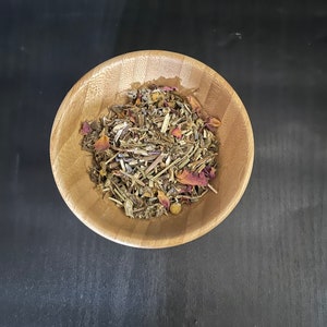 May include: A wooden bowl filled with dried herbs and rose petals. The bowl is on a black surface.