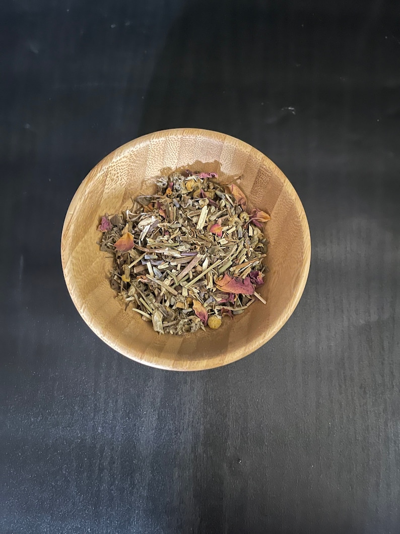 May include: A wooden bowl filled with dried herbs and rose petals. The bowl is on a black surface.