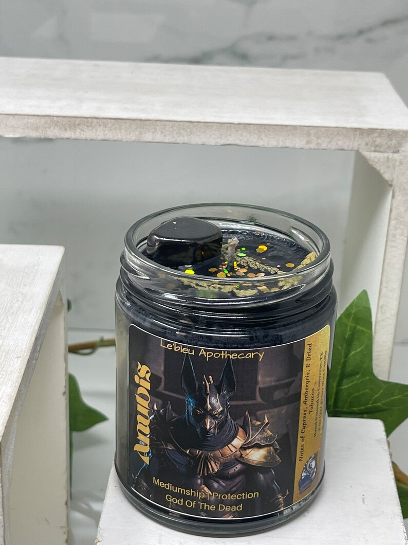 May include: Black candle jar with a gold label that reads "Anubis Mediumship Protection God Of The Dead Le'bleu Apothecary Notes of Cupress, Ambergris, & Dried Tobacco".
