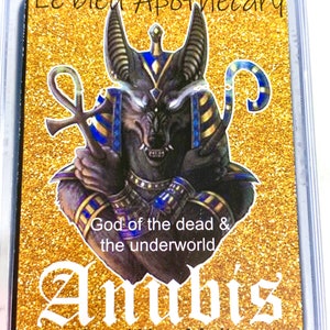 May include: A gold and black wax melt with a graphic of Anubis, the Egyptian god of the dead, with the text "Le'bleu Apothecary", "God of the dead & the underworld", "Anubis", "Soy Wax Melts", and "Net wt. 3 Oz".
