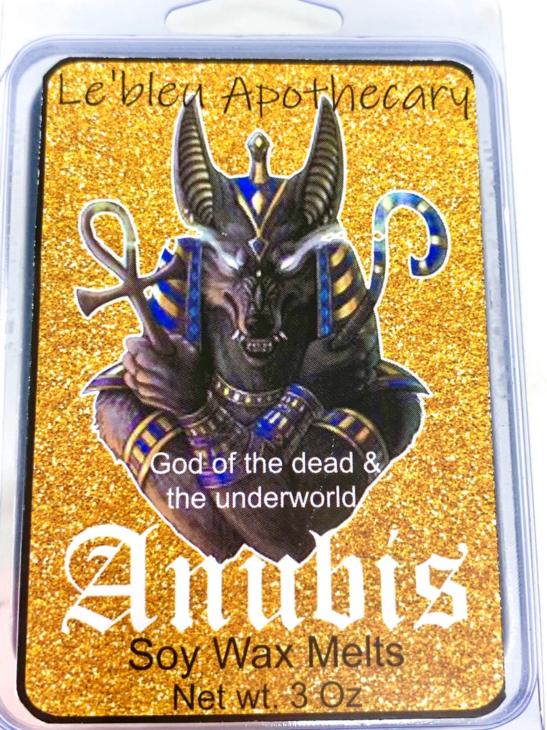 May include: A gold and black wax melt with a graphic of Anubis, the Egyptian god of the dead, with the text "Le'bleu Apothecary", "God of the dead & the underworld", "Anubis", "Soy Wax Melts", and "Net wt. 3 Oz".