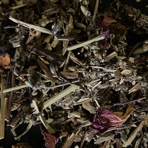 May include: A close-up of a mixture of dried herbs and flowers, including lavender, rose petals, and other botanicals. The mixture is a light brown color with hints of purple and pink.