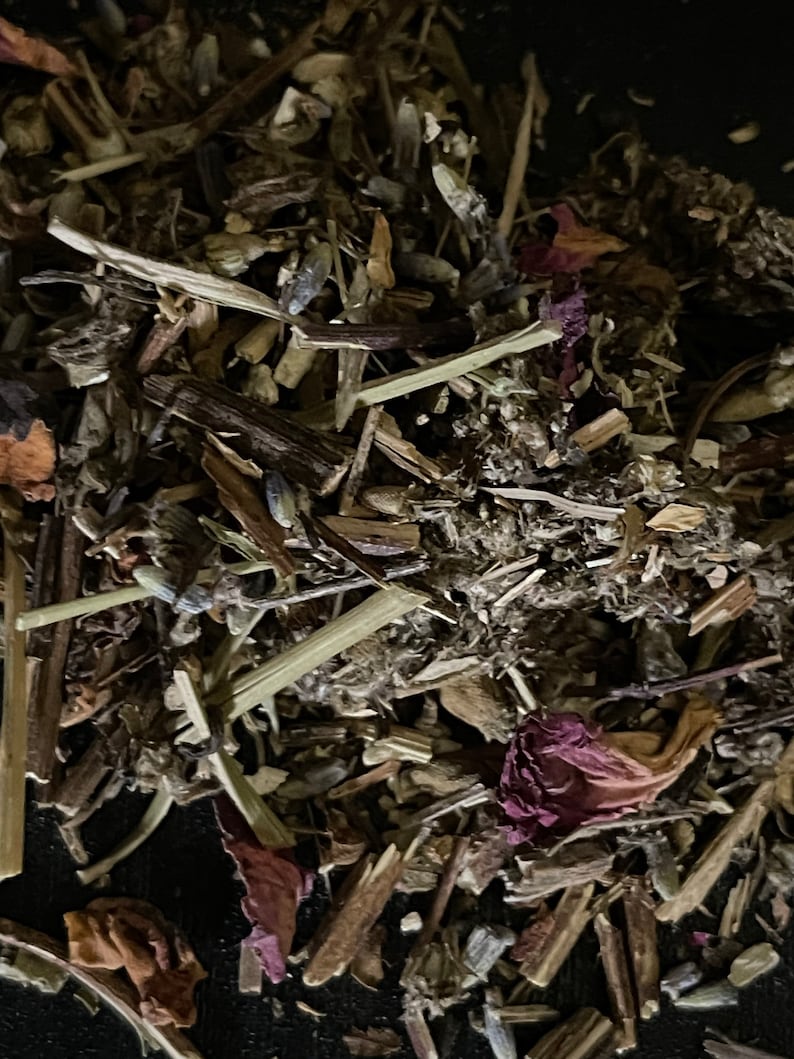 May include: A close-up of a mixture of dried herbs and flowers, including lavender, rose petals, and other botanicals. The mixture is a light brown color with hints of purple and pink.