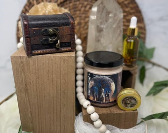 Puede incluir: Una caja de madera con un cierre de latón, un cristal blanco, una vela con una etiqueta negra que dice "Incienso" y "Leila Apothecary", un pequeño frasco con hierbas secas y un collar de cuentas blancas.