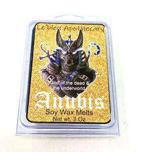 May include: A gold and black wax melt container with an image of Anubis, the Egyptian god of the dead. The container is labeled "Le'blen Apothecary" and "Anubis Soy Wax Melts Net wt. 3 Oz".
