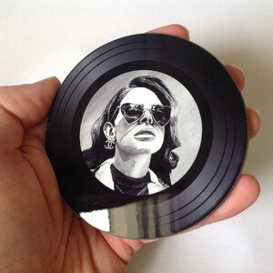 May include: Black and white illustration of a woman wearing heart-shaped sunglasses on a black vinyl record coaster.