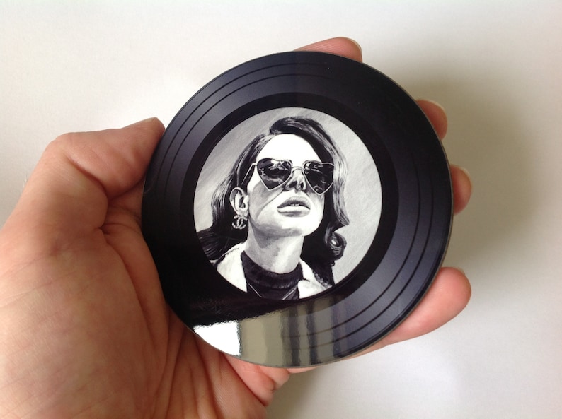 May include: Black and white illustration of a woman wearing heart-shaped sunglasses on a black vinyl record coaster.
