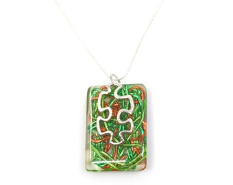 May include: A silver chain necklace with a rectangular pendant. The pendant is filled with green and orange wire and features a silver puzzle piece charm.