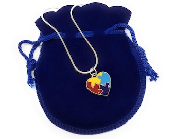 May include: A silver chain necklace with a blue, yellow, red, and purple puzzle piece heart pendant. The necklace is in a blue velvet pouch.