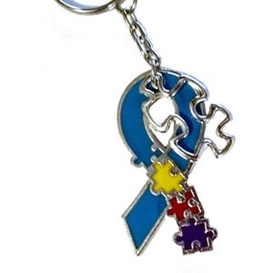 May include: A blue ribbon keychain with puzzle pieces in yellow, red, and purple. The ribbon is a symbol of autism awareness.