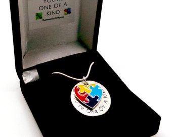 May include: A silver necklace with a heart-shaped pendant featuring a colorful puzzle piece design. The pendant is engraved with the text "You're One Of A Kind". The necklace is displayed in a black velvet box.