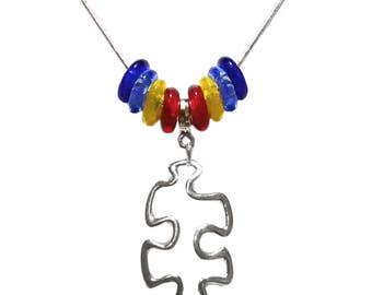 May include: A silver chain necklace with a silver puzzle piece pendant. The chain has blue, yellow, and red glass beads.