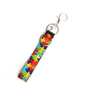 May include: A black key chain with a silver clip and a colorful puzzle piece pattern.