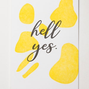 May include: A white card with the text "hell yes." printed in black. The card is decorated with yellow abstract shapes.