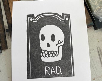 May include: Black and white print of a skull with the word "RAD." printed below it.