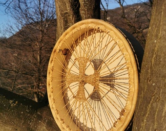 Può includere: Un tamburo a cornice rotondo in legno con una pelle bianca in cuoio. Il tamburo è decorato con un motivo intrecciato di corda marrone.